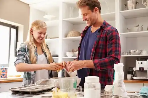 A father and a daughter are happily making a cake in the kitchen.