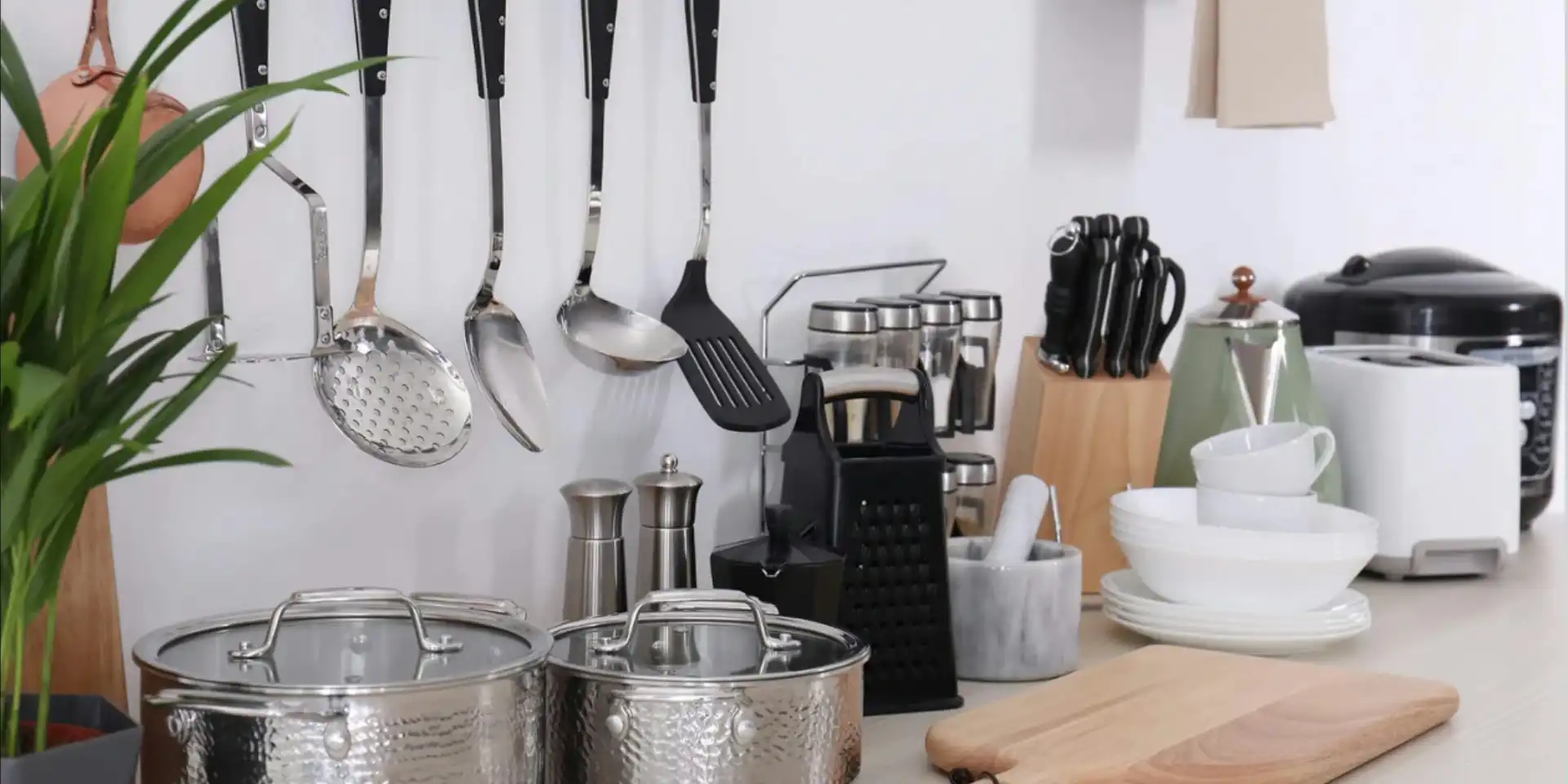 Some kitchenwares are placed on the countertop and some kitchen utensils are hung on the wall