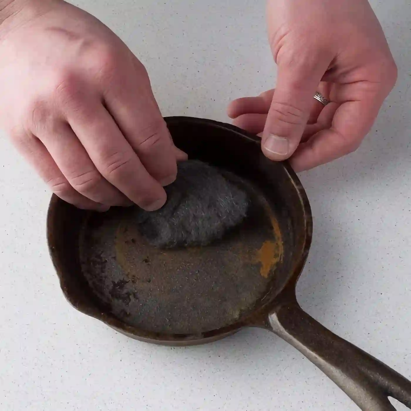 man hands clean rusty frying pan with steel wool