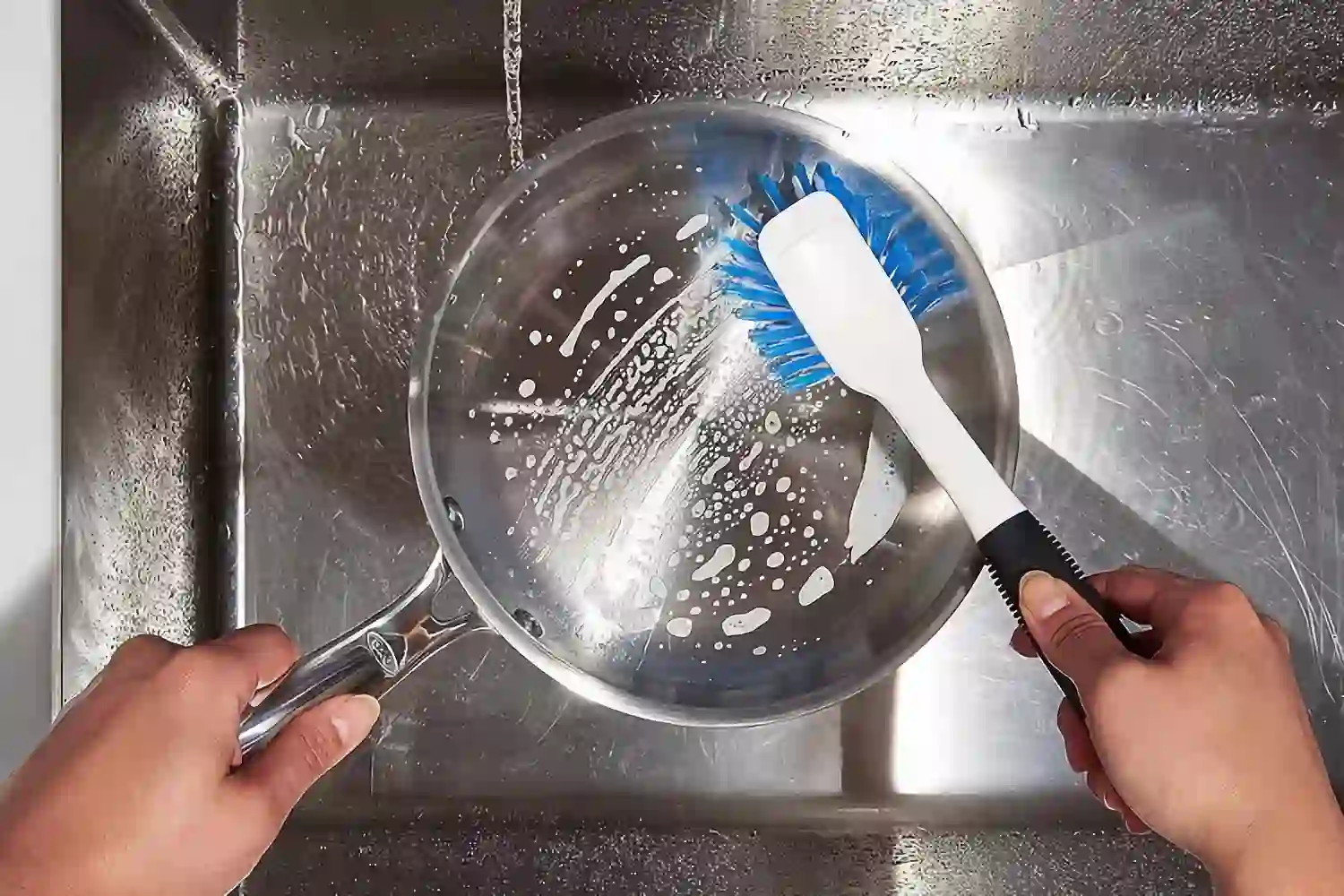 A person cleans the stainless steel pan with a grip dish brush