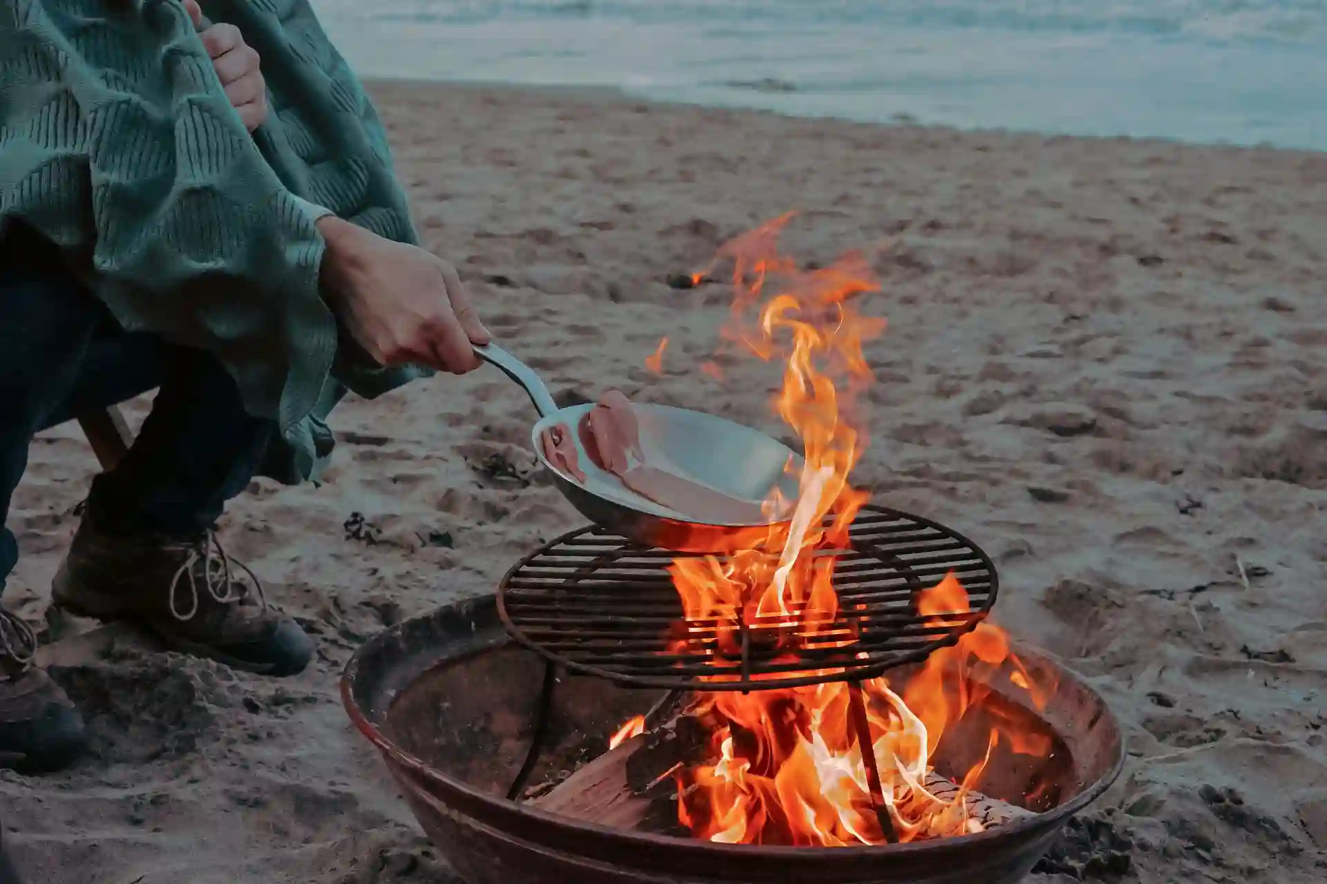 Person cooking meat on bonfire near shoreline