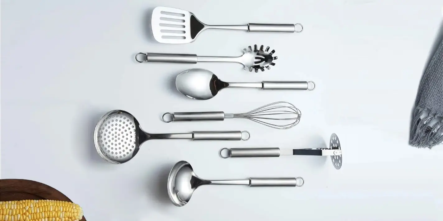 Stainless steel kitchen cooking utensils set against light grey background