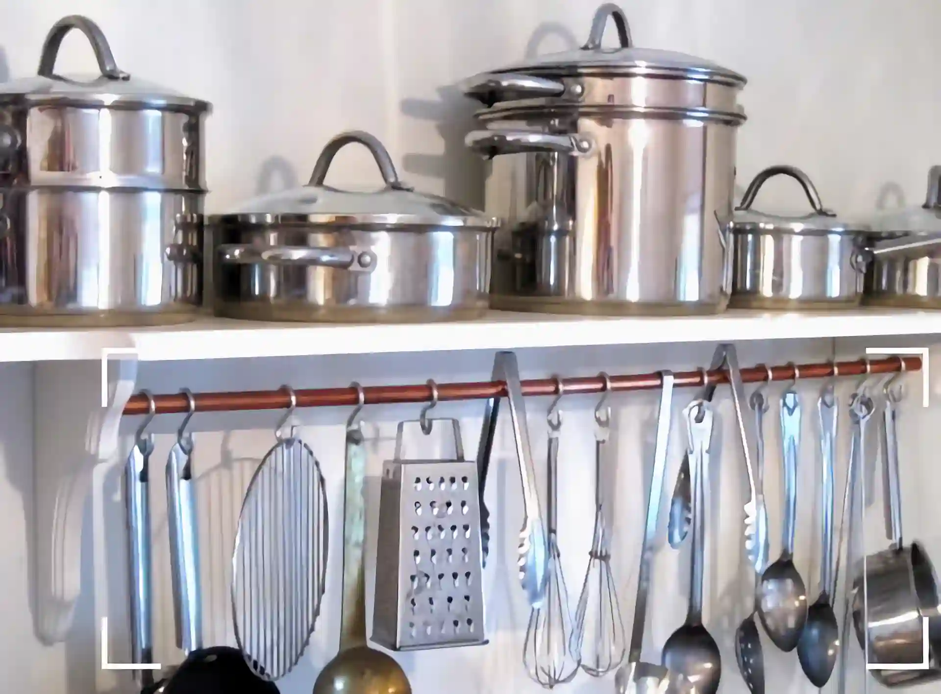 Floating shelves are filled with stainless steel cookware, the wall-mounted rails under the shelves are hang of stainless steel kitchen utensils