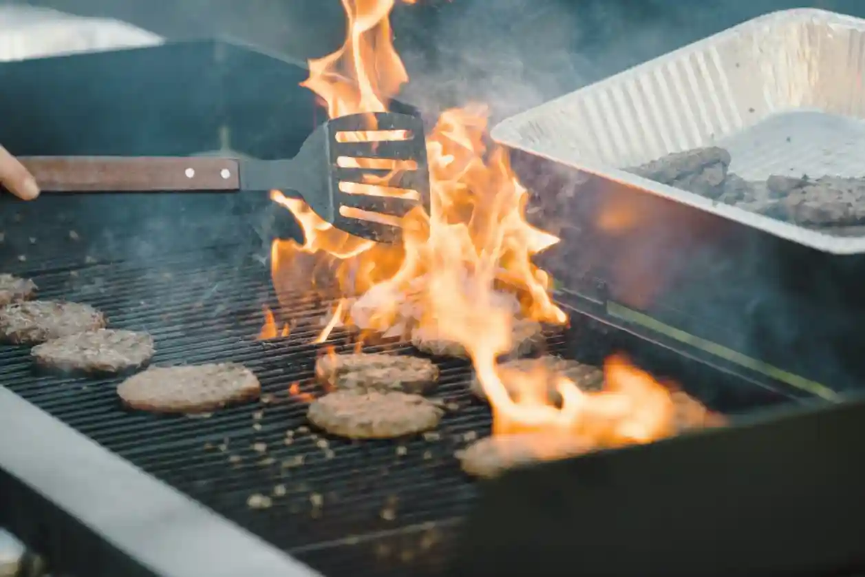 A person grilling hamburgers and hamburger patties on a grill