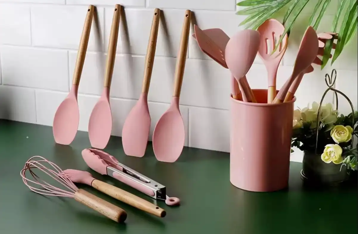 Pink nylon kitchen utensils with wooden handle sit on a green countertop