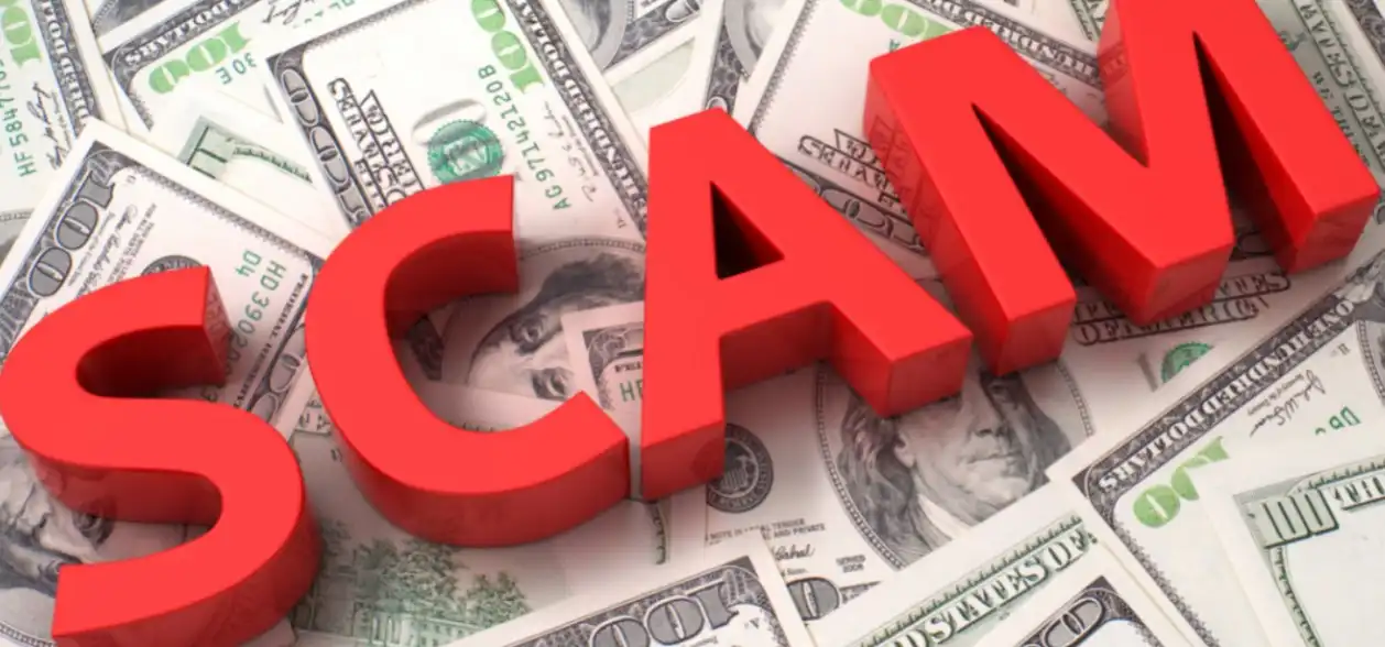 A word “scam” consisting of red letter blocks placed on a pile of U.S. currency